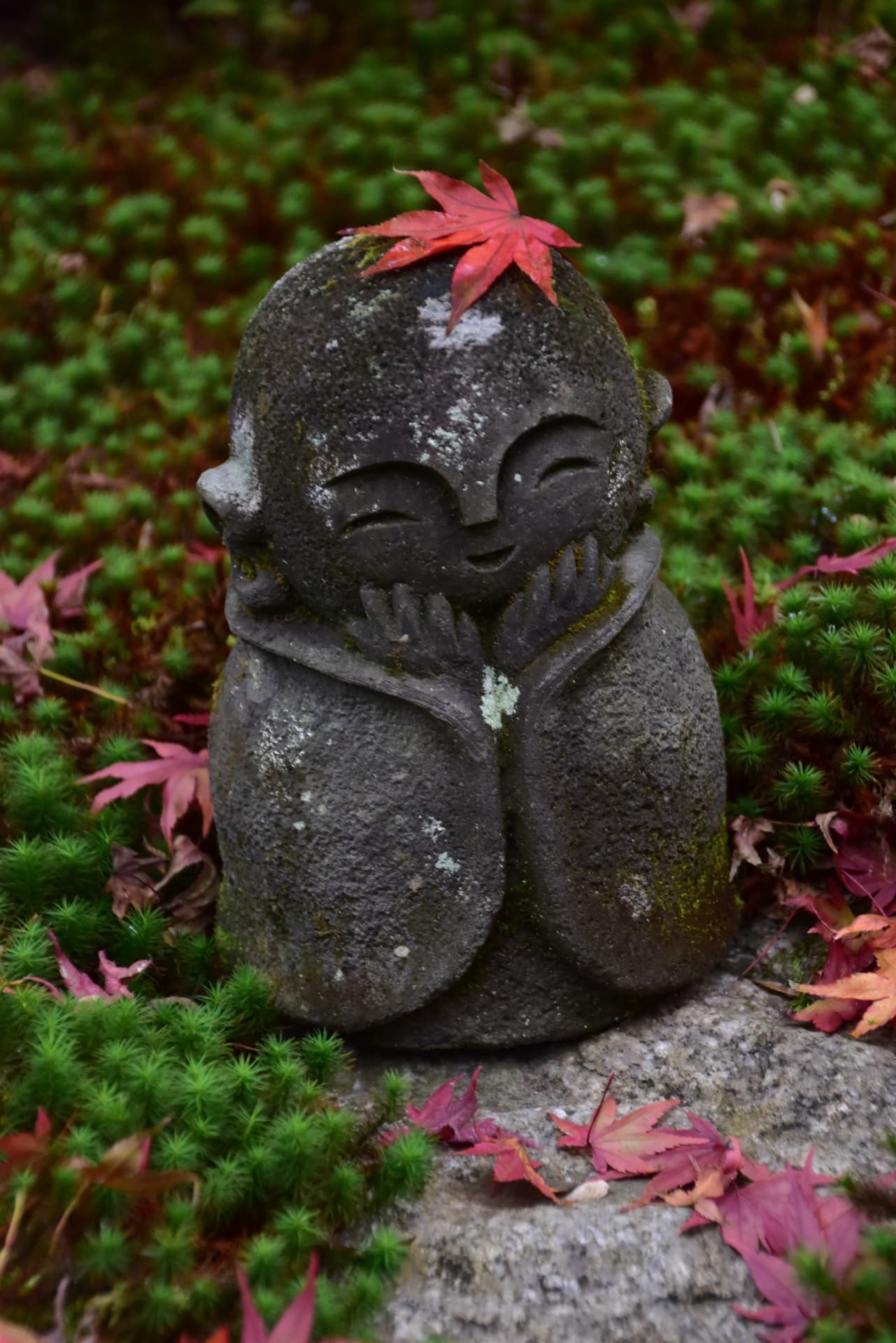 One red maple leaf on a smiling jizo